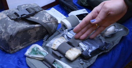 Woman’s hand showing content of an Ukrainian soldier’s first aid kit: bandages, wound-healing drugs, tourniquet, painkillers